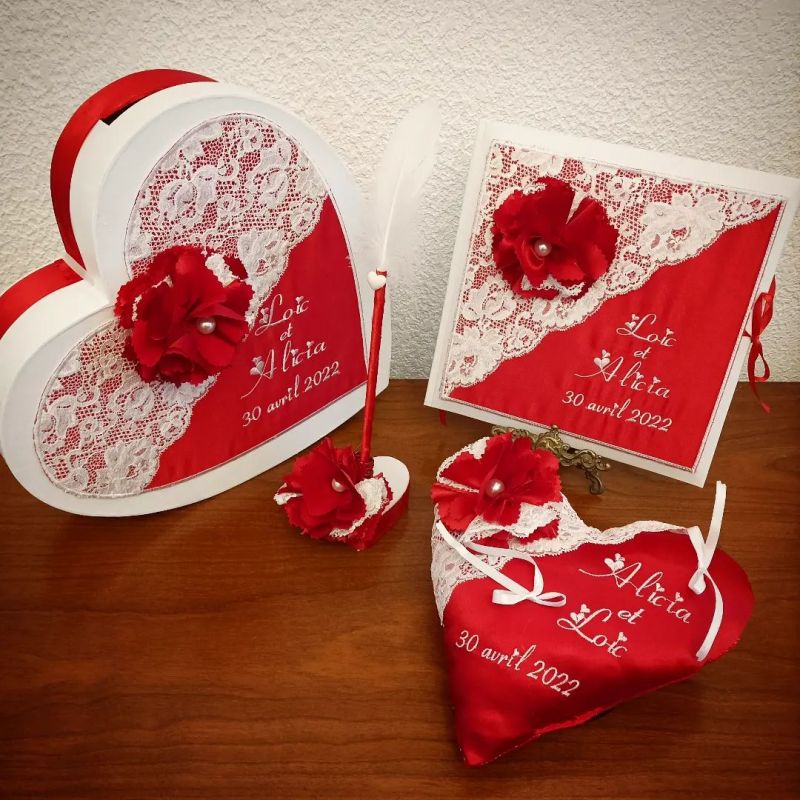 Déco de mariage dans les tons rouges comprenant une urne en forme de coeur, un livre d'or, un porte-alliances, un stylo